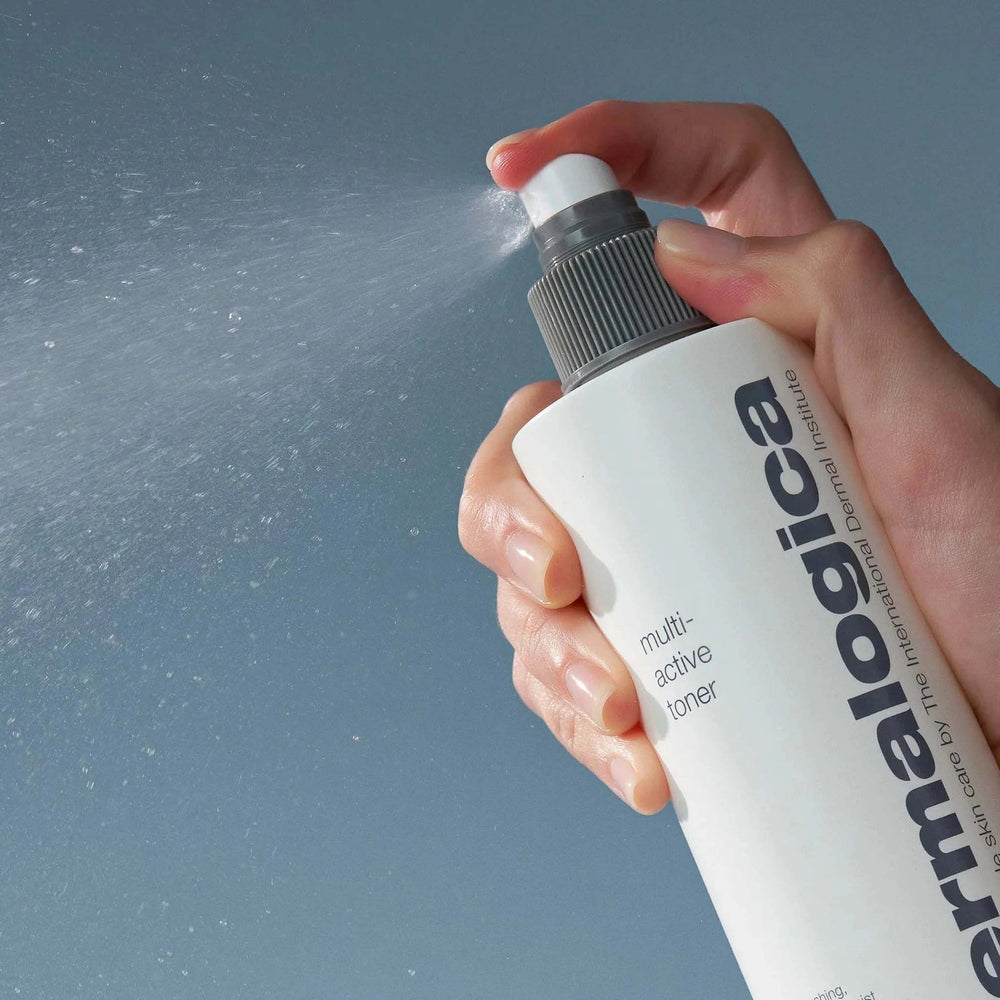 Hand holding a bottle of Dermalogica multi-active toner spraying it against a gray background